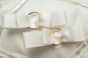 Anelli d'oro legati elegantemente con fiocco largo sopra cuscinetto bianco