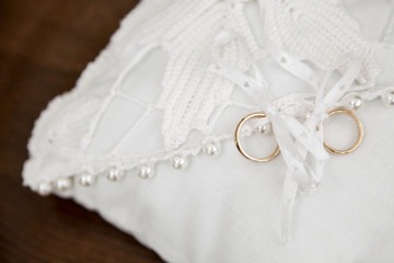 Anelli d'oro legati sopra cuscinetto bianco con perle ripreso dall'alto