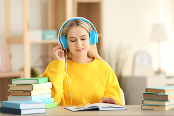 Young woman sitting at table and listening to audio book