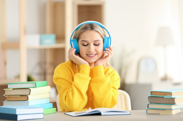 Young woman sitting at table and listening to audio book