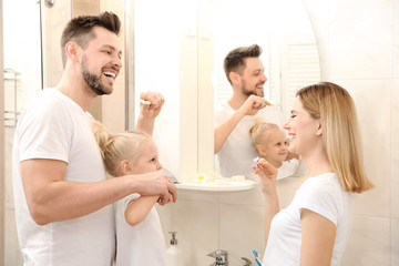 Young couple and their beautiful daughter brushing teeth near mirror in bathroom