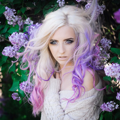 close-up portrait of a beautiful sexy young blonde girl hipster with lilac and pink hair on the background of blooming lilacs, posing