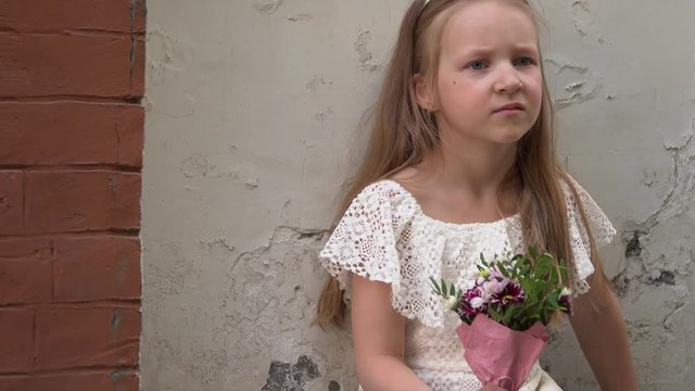 The little girl costs at a brick wall in a pink dress and with a small bouquet of beautiful flowers