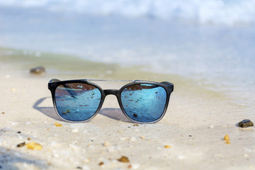 Fashion blue sunglasses on sandy  beach near the blue sea. Summer holiday concept