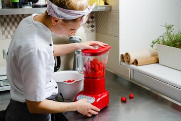 Woman grind strawberries in a red blender