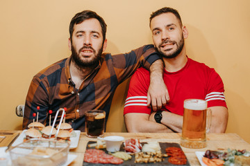 .Two male friends watching football in a bar, having beer and something to eat having a good time. Lifestyle portrait