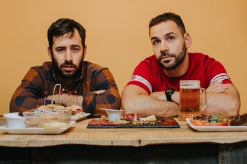 .Two male friends watching football in a bar, having beer and something to eat having a good time. Lifestyle portrait
