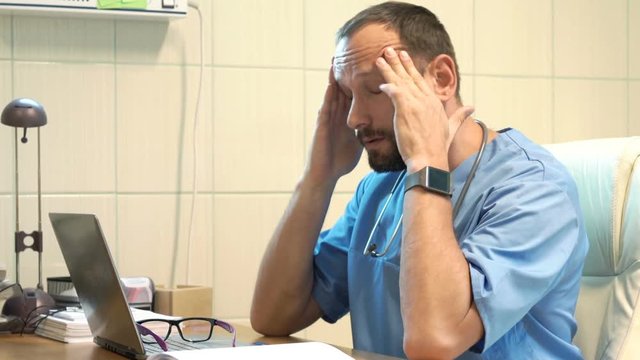 Male doctor having head pain while working on laptop in office
