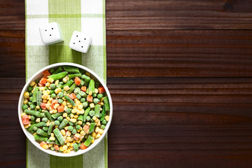 Frozen mixed vegetables (green bean, pea, carrot, sweet corn) in bowl, photographed overhead on dark wood with natural light