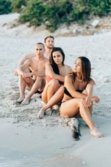 Fototapeta premium Group of friends millennials wearing swimsuits sitting on the beach outdoor looking at view - getting away from it all, serene, thinking future concept
