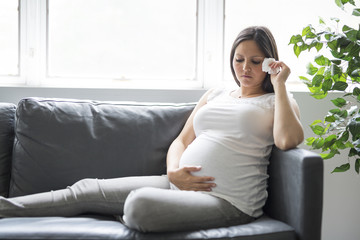 Sad pregnant woman lying on sofa at home