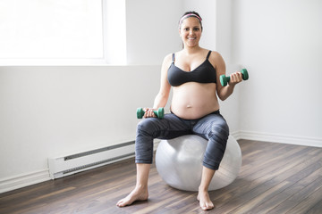 Fototapeta na wymiar Pregnant woman training with dumbbells to stay active