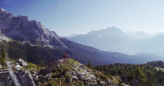 Aerial flight above people hiking along trail path in sunny day. Group of friends summer adventure journey in mountain nature outdoors. Travel exploring Alps, Dolomites, Italy. 4k drone orbit video