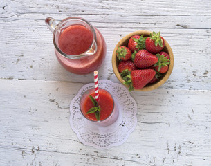 Delicious homemade strawberry smoothie on rustic white wooden background