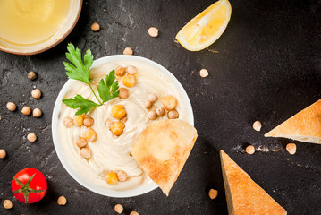 Healthy food. Vegetable sources of protein. Bowl of hummus, on black stone table, with greens, boiled and raw chickpeas. With fresh cucumber, tomatoes, carrots and bread pita. Copy space top view
