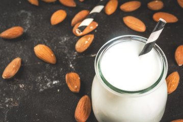 Vegetable sources of protein. Vegan healthy food. A small bottle of almond milk, portion. Against the backdrop of nuts, almonds, on a black concrete table. Selective focus. Copy space