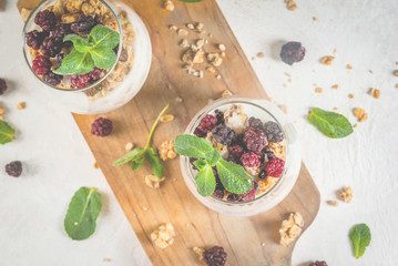 Dietary vegan healthy breakfast. Yogurt and granola with fresh blackberry oranges and mint in a glass. On a white table, on a cutting board. Copy space top view