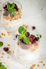 Dietary vegan healthy breakfast. Yogurt and granola with fresh blackberry oranges and mint in a glass. On a white table. Copy space close view