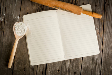 Baking background. Tools and ingredients for baking on the old rustic wooden table. Book notepad...