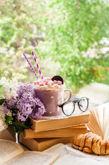 Coffee cup with marshmallow, open book, glasses, croissant and flowers bouquet on window sill. Breakfast, reading and education concept