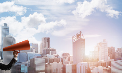Naklejka premium Hand of businesswoman holding red paper trumpet against cityscape background