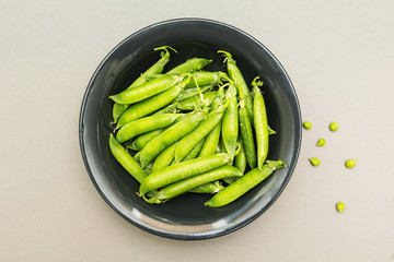 A plate of organic peas in pods on a gray background, the top view.