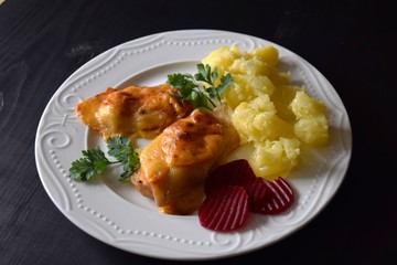 Chicken breast baked with cheese on a white plate, wooden board, close up view