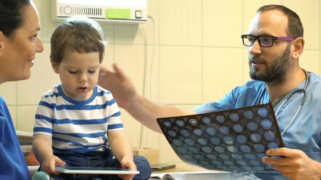 Doctor With Brain Scan In Office Talking Good News To Mother With Child
