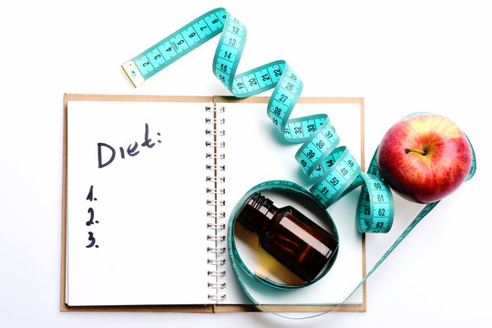 Notebook with diet plan, twisted blue measuring tape on it