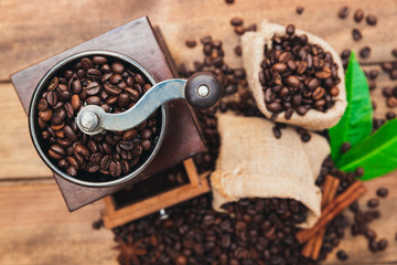 Cup of coffee with sack full of roasted coffee beans and coffee mill on wooden table