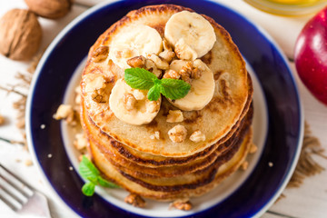 Pancakes with banana, honey, walnuts and mint on plate.