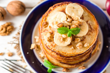 Pancakes with banana, honey, walnuts and mint on plate.