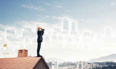 Fototapeta na wymiar Engineer man standing on roof and looking in binoculars. Mixed m