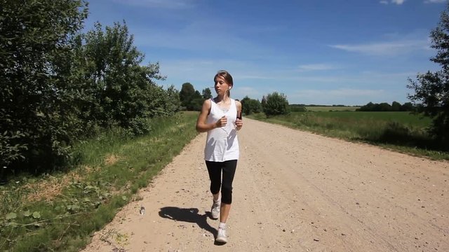 Beautiful teenage girl running on the road on sunny summer day.Young beautiful girl running and listening to music with headphones.