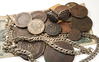 Antique silver, silver and bronze coins and jewelry lying on old banknotes. On the white background.