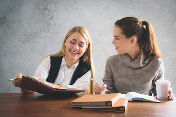 Two young european business women are sitting on the table and discussing about their work or project