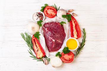 Raw meat with herbs, spices and seasoning on white wooden background, ingredients for cooking, top view. Beef meat with vegetables for soup or steak