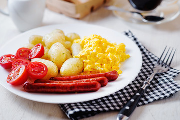 Traditional American breakfast, hotel or restaurant, boiled potato with dill, smoked sausage, omelette from chicken eggs, fresh cherry tomato, white toast, milk and black coffee on a light background