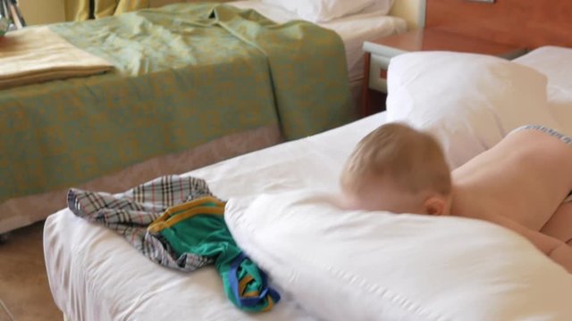 Cute toddler boy playing with pillow on bed and laughing. He throws it and falls next to it.