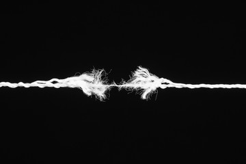 Tearing white the rope in the middle of the frame on the black background