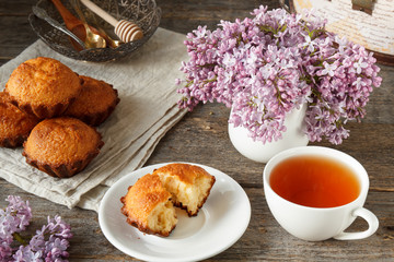 Cupcake on a plate, Cup of tea, a bouquet of lilacs, a few muffins. Wooden background.