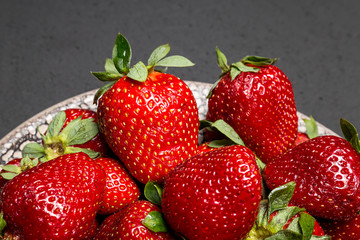 fresh ripe useful fruit strawberry in a clay bowl closeup on a black background