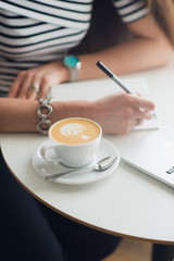 Close-up hands of woman holding a pen over empty notebook with cup of coffee next to it. Top view composition. Workplace of office female.