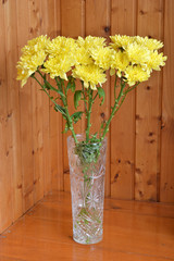 Bouquet of yellow chrysanthemums in a crystal vase on the table on the background of wooden wall
