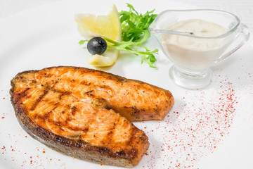 A delicious large piece of fried fish with sauce, lemon and herbs. Horizontal frame