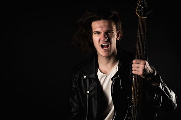 Music and creativity. Handsome young man in a T-shirt, jacket and jeans, with an electric guitar, on a black isolated background. Horizontal frame