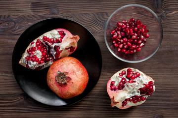 plate of fresh red pomegranate sliced fruit with seeds wooden background top view