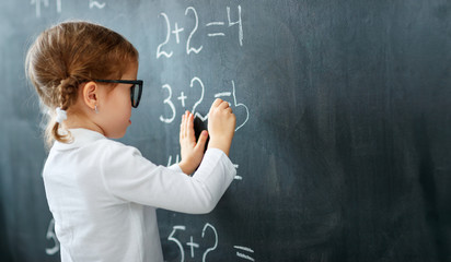 Happy schoolgirl preschool girl with book near school blackboard