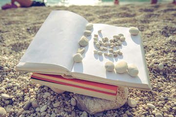 Naklejka na ściany i meble Open book at the beach near the sea during a summer holiday on a sunset
