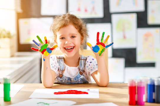 funny child girl draws laughing shows hands dirty with paint